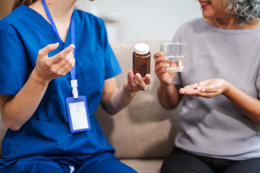 Caucasian female doctor provides a glass of water and medication pills to an elderly Asian